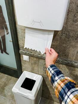 A person is engaging in the action of pulling a roll of toilet paper out from inside a paper towel dispenser that is designed for easy access to paper products when needed photo