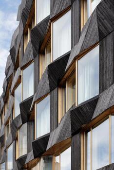 Architectural facade showcasing unique burnt wood color with angular design elements and large windows, creating a striking visual impact in modern architecture photo