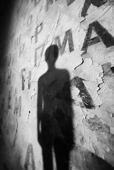 Shadow of a person cast on a peeling wall with visible textures and letters, creating a dramatic contrast and evoking a sense of mystery and depth in the scene photo