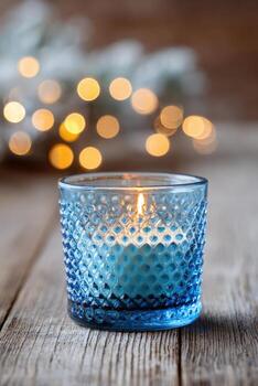 Textured candlelight still life featuring a blue glass holder, illuminating a warm ambiance with soft bokeh lights in the background, creating a serene and inviting atmosphere photo