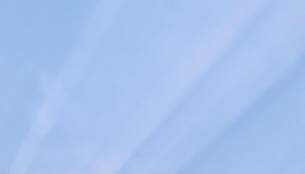 Subtle crepuscular sun rays stretch diagonally across a soft, pale blue sky, creating a minimalist and serene atmospheric background with maximum copy space. photo