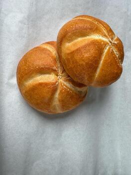 Two fresh golden Kaiser rolls on parchment paper, top view bakery background photo