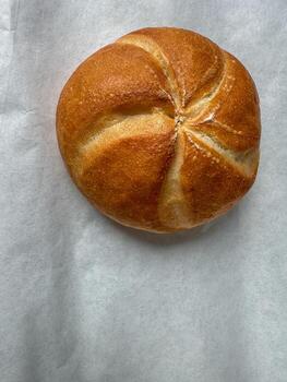 Fresh golden Kaiser roll on parchment paper, top view bakery food background photo