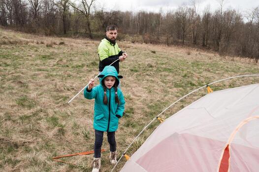 Setting up a cozy campsite on a cloudy day in early spring with a child learning the art of camping and bonding with nature in a lush green field photo