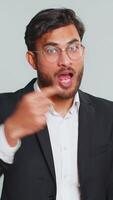 Eu escolher você. indiano sorridente homem de negocios apontando dedo para Câmera e olhando com brincalhão feliz expressão, fazer vencedora escolha, mostrando direção. árabe homem isolado em cinzento estúdio fundo video