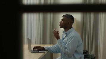 pov espião ponto do Visão africano americano homem cara masculino do utilizador trabalhador autonomo aluna o negócio homem trabalhando o negócio atrasado noite tarde às casa pensando pensativo digitando computador portátil pensar resolução problema autor trabalhos video