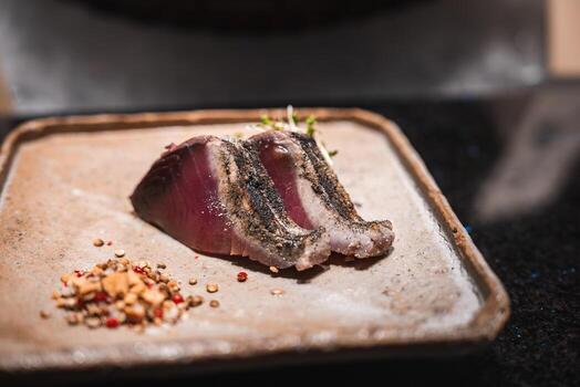Two seared tuna slices with charred crust rest on stoneware in Japan, with crushed spices and microgreens. Soft focused light highlights texture and refined plating. photo