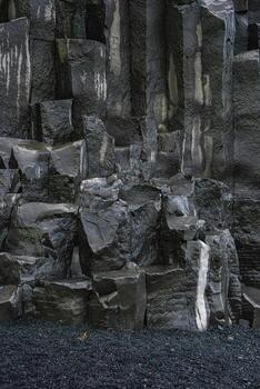 Close view of hexagonal basalt columns at Reynisfjara near Vik in Iceland. Dark rock with pale veins rises above black sand under overcast light, with sharp edges. photo