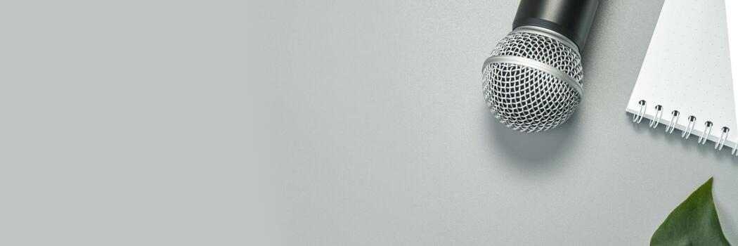 Microphone on gray surface with notebook and leaf for audio recording or podcast setup. photo