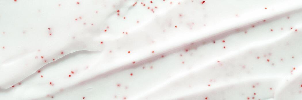Close-up of white cream with red particles creating texture and patterns on smooth surface. photo