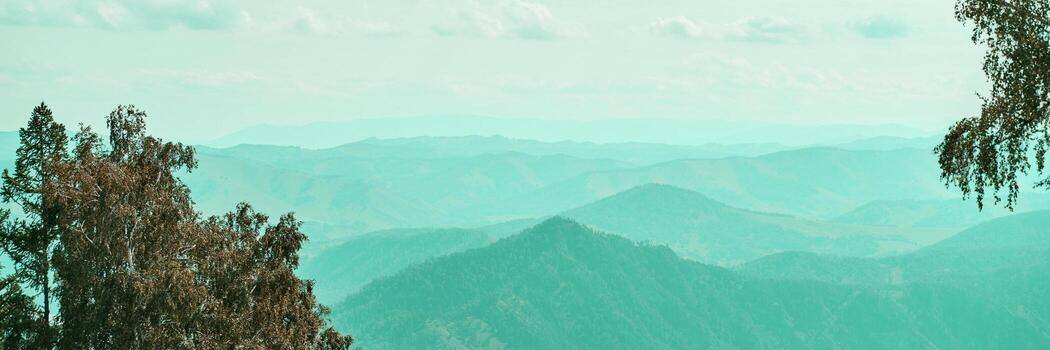 Expansive mountain range view with trees in foreground under cloudy sky. photo