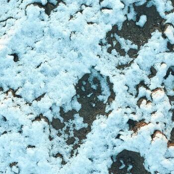 Snow-covered ground showing uneven patterns of white snow on dark soil creating a natural winter texture. photo