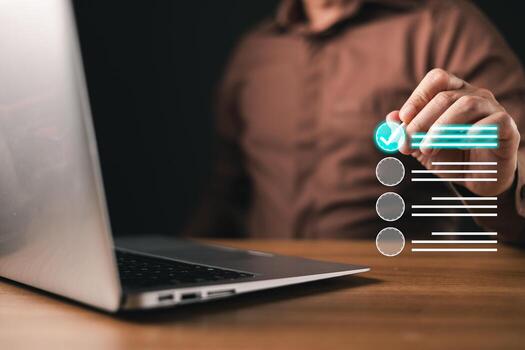 A man interacts with a futuristic digital checklist, marking tasks as completed. A laptop sits on the desk, symbolizing technology, productivity, business management, and workflow efficiency. photo