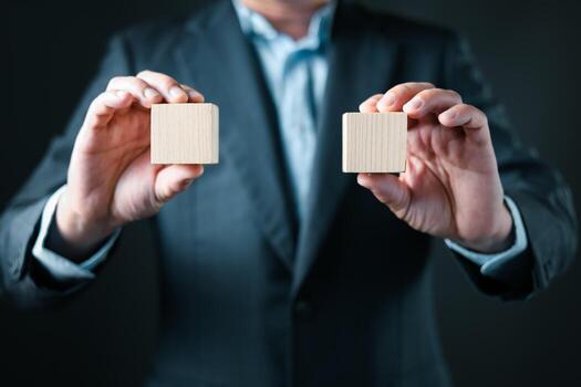 A person in a business suit holds two identical wooden blocks in both hands, symbolizing comparison, decision making, equality, and strategic business choices in a minimalist setting. photo