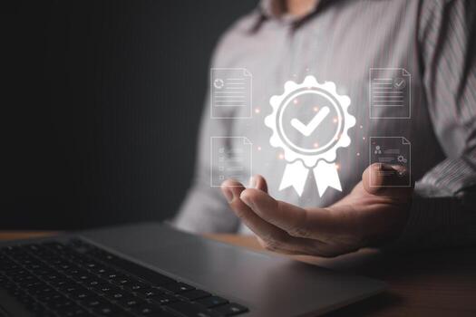 A person holds a glowing quality control badge hologram featuring a checkmark and surrounding digital document icons, symbolizing certification, standards, and reliable assurance in modern processes. photo