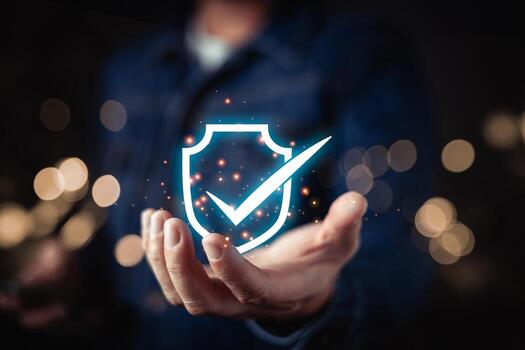 A person presenting a glowing blue shield icon with a checkmark, symbolizing cybersecurity, data protection, and trust in secure digital systems within a modern technological framework. photo