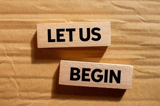 Let us begin message written on wooden blocks on cardboard background. Conceptual let us begin symbol. Copy space. photo