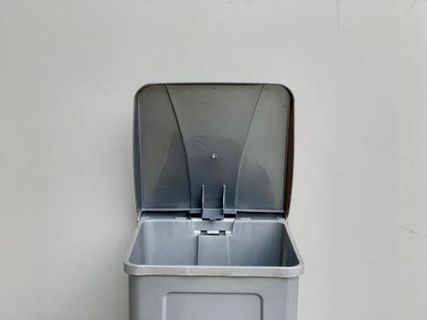 Gray Plastic Trash Can with Open Lid Against a Plain Wall. photo