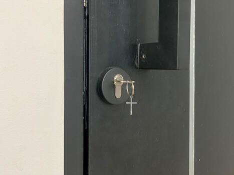Closeup of a modern black door with a key in the lock featuring a crossshaped keychain. photo