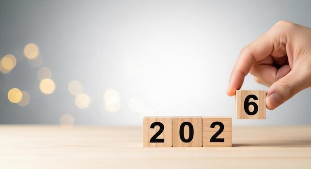 A hand is placing a block the transition to the year 2026 against a soft, blurred background. photo