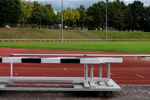 A track field features hurdles placed on the red running surface. In photo
