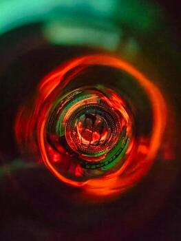 Close-up abstract image taken from inside a glass bottle, showcasing vivid red and green light reflections. Strong circular symmetry and bokeh effect. Ideal for creative, surreal, or artistic concepts photo