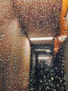 Raindrops clinging to a glass window, creating a soft, textured effect with blurred indoor lighting in the background. reflecting blurred orange and gray hues of passing scenery. photo