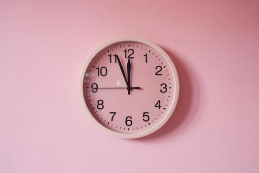 Simple wall clock showing time close to twelve on a pink background in a cozy room setting photo