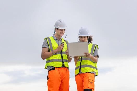 Construction or Industrial Engineers Team Reviewing Project Data, Safety Managers Communicating and Planning with Laptop, Field Workers in High-Visibility Vests Using Technology on Site photo