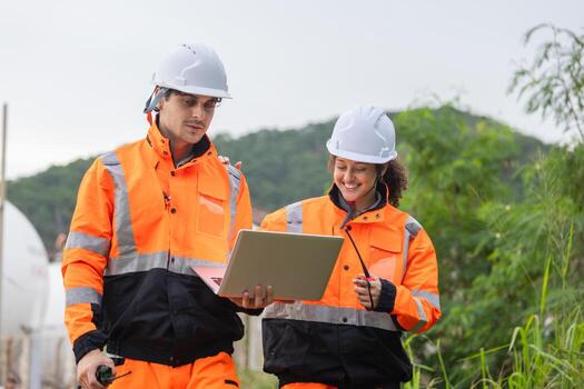 Industrial Engineers Collaborating with Laptop and Walkie Talkie, Happy Construction Workers Reviewing Project Plans Outdoors, Safety Team Discussing Field Operations with Digital Device photo
