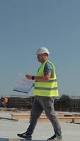 architetto rivedere progetti a moderno costruzione luogo. un architetto nel un' riflessivo veste e casco esamina edificio progetti mentre a piedi attraverso un' video
