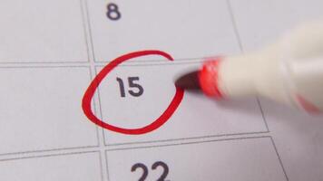 The 15th on the calendar is circled in red marker in a close-up macro shot on a white page, symbolizing an important day or reminder. video
