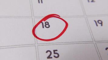 il 18 ° su il calendario è cerchiato nel rosso marcatore nel un' avvicinamento macro tiro su un' bianca pagina, simboleggiante un importante giorno o promemoria. video