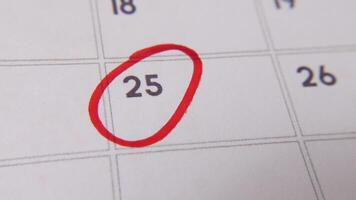 il 25 su il calendario è cerchiato nel rosso marcatore nel un' avvicinamento macro tiro su un' bianca pagina, simboleggiante un importante giorno o promemoria. video