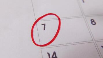 il 7 ° su il calendario è cerchiato nel rosso marcatore nel un' avvicinamento macro tiro su un' bianca pagina, simboleggiante un importante giorno o promemoria. video