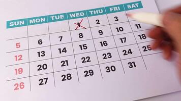 en hand märkning av datum på en vägg kalender med en röd markör, representerar schemaläggning, deadlines, eller tid förvaltning. video