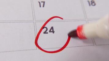 de 24:e på de kalender är ringade in i röd markör i en närbild makro skott på en vit sida, symboliserar ett Viktig dag eller påminnelse. video