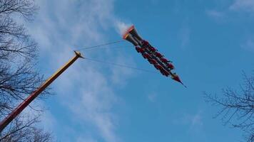 Exhilarating low-angle shot focusing on the The Rocket themed extreme pendulum ride as it reaches its apex, emphasizing the height and speed. Passengers are strapped into the multiple red seats video