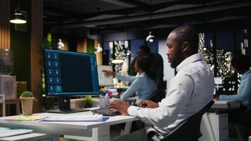 African american male checking web AI chatbot responses for some tasks, working after hours to meet business objectives. Problem solving with futuristic tech and machine learning. Camera A. video