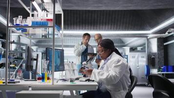 afrikansk amerikan forskare placering bricka under de mikroskop, diabilder materia för molekyl och genetik forskning. optik, diagnostik och analys med Avancerad Utrustning för biokemi. kamera a. video