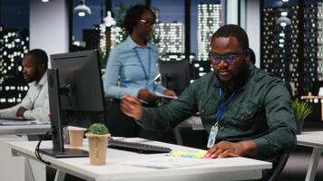 negro negocio persona colocación un pegajoso Nota recordatorio en monitor, utilizando adhesivo papel etiqueta a recuerda un nuevo desarrollo tarea. oscuro oficina a noche, motivación para eficiencia. cámara b. video