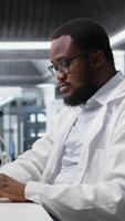 vertikal laboratorium arbetstagare vindögd ögon på dator övervaka, kämpar till förstå dna data. afrikansk amerikan labb expert- oförmögen till tro ögon medan ser på genetisk analys diagnostik, kamera en video