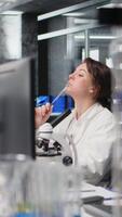 Vertical Laboratory scientist brainstorming ideas at computer desk, rubbing pen on chin, waiting for data to be processed. Woman in lab doing thinking, interpreting lab genetic analysis diagnostics, camera A video