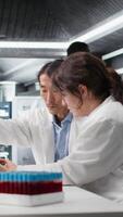 vertikal laboratorium chef och praktikant använder sig av läsplatta app till bearbeta dna patient data för klinisk forskning. labb team ledare och internera använda sig av enhet till do labb genetisk analys diagnostik, kamera en video