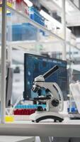 Vertical Computer monitor in biotechnology laboratory showing molecular model visualization and microscope on workbench. Bioengineering software on PC in medical lab displaying DNA data and optical device video