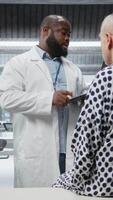 Vertical Black scientist observes patient reactions during a drug trial in a healthcare institute, recording data and monitoring vitals to ensure safe dosage levels for progress in medicine. Camera A. video