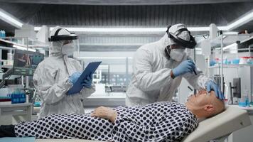 sjukvård professionell i hazmat kostym utför diagnostik på en patient smittad med farlig virus, studerar immunitet och vaccination svar i en säkra bioinneslutning miljö. kamera a. video