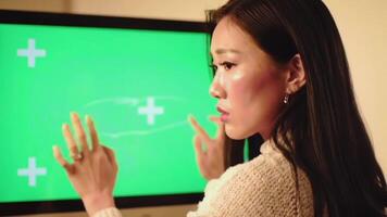 en kvinna användningar hand gester till slägga och kontrollera en stor interaktiv grön skärm. en perfekt attrapp för visning trogen data, ui, eller ar och vr innehåll. video