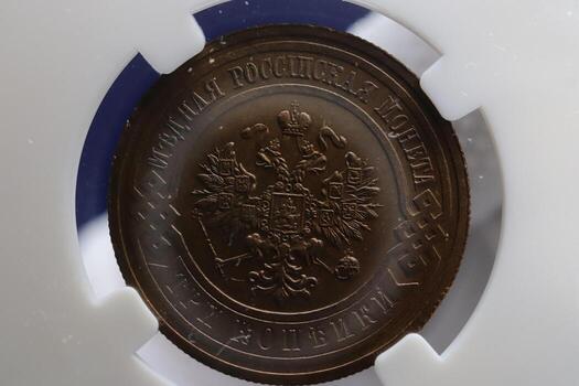 A bronze coin featuring a detailed emblem with a double-headed eagle and royal insignia, encapsulated in protective casing photo