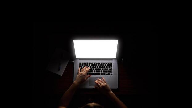 Overhead hacker in the hood working with laptop and mobile phone typing text in the darkroom. photo